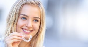 a young woman smiling while holding a chester county invisalign aligner